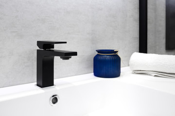 Gray bathroom interior with white sink black modern techno style faucet blue glass jar and white...