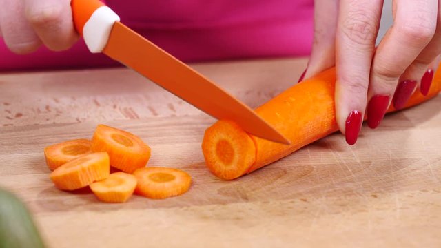 Close up of woman hand cutting chopping carrot on kitchen board using cooking knife in slow motion.