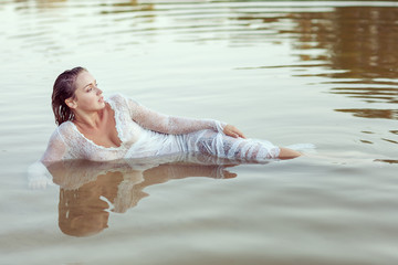 Beautiful woman in white dress lies in the water on the beach.