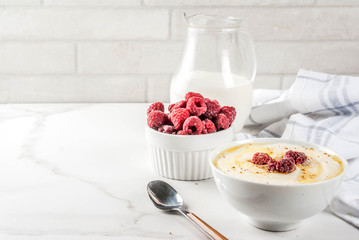 Healthy breakfast, semolina porridge with milk and raspberry, white marble table copy space
