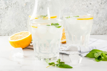 Summer refreshing drinks, mojito or lemonade with fresh mint, slices of lemon, ice, on a light background. copy space