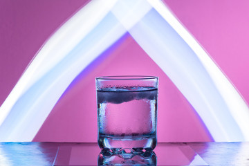 Liquid with ice in a glass on a reflective surface on a reddish background