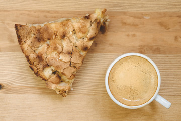 Top view of white coffee cup filled with fresh hot espresso together with peace of freshly baked homemade apple pie on wooden background