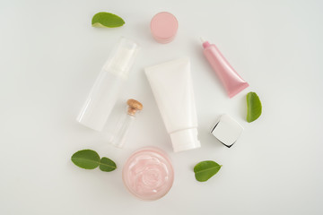 White cosmetic products and green leaves on white background. Natural beauty blank label for branding mockup concept.