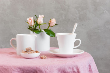 The white cup of tea or coffee with milk on the table coated with pink tablecloth