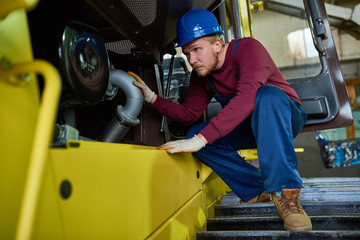 Full length portrait of handsome young worker wearing overall and hardhat sitting on haunches while...