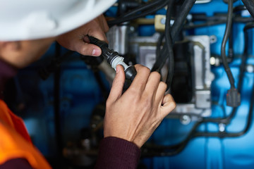 Close-up shot of young technician wearing protective helmet repairing hydraulic excavator system at spacious heavy equipment factory