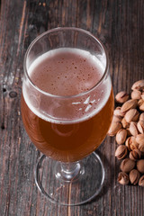 A glass of refreshing light beer and a scattered handful of pistachios on a table of old textured wooden boards.