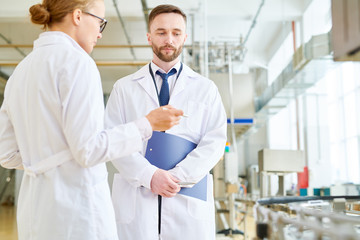 Highly professional technologist explaining something to bearded inspector while giving tour around...