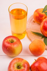 A glass of apple-peach juice and ripe fresh fruit on a light background