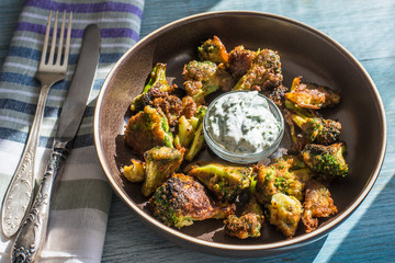 Fried broccoli in batter with spicy white sauce in a plate on a rustic background - top view