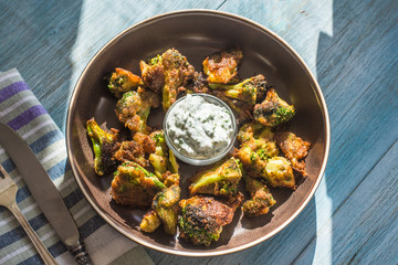 Fried broccoli in batter with spicy white sauce in a plate on a rustic background - top view