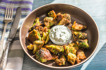 Fried broccoli in batter with spicy white sauce in a plate on a rustic background - top view
