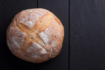 Round bread on a black background, bread from a stove on dark boards, a dough for a designer, copy space, rustic style, minimalism, top view, bakery