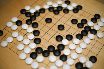 Go East game. Traditional Chinese game. wooden board "goban" with black and white stones. A tree lined with stripes squares intersection of strips. «I-go» «Go» game