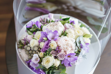 Flower in transparent plastic box. Brides wedding bouquet with peonies, freesia and other flowers on black arm chair. Light and lilac spring color. Morning in room