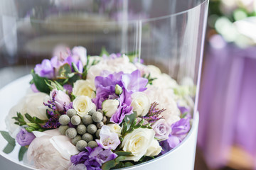 Flower in transparent plastic box. Brides wedding bouquet with peonies, freesia and other flowers on black arm chair. Light and lilac spring color. Morning in room