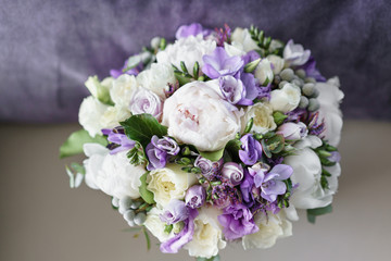 Brides wedding bouquet with peonies, freesia and other flowers on black arm chair. Light and lilac spring color. Morning in room
