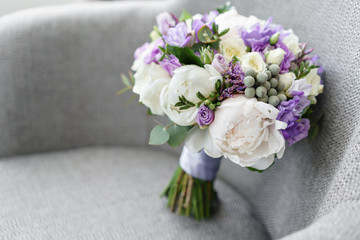 Brides wedding bouquet with peonies, freesia and other flowers on black arm chair. Light and lilac spring color. Morning in room