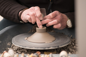 man using tool to make clay pot before firing