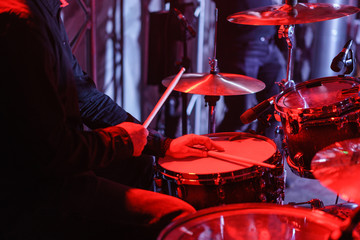 Fototapeta na wymiar Drummer playing on drum kit on stage. Close-up of plate, drums, sticks, in background scene spotlights