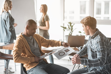 Obraz premium Two men taking seat in office. They looking at statistical data on paper. Female partner on background