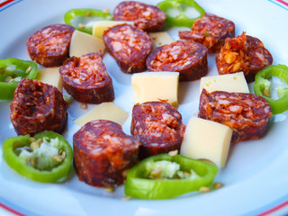 Hungarian breakfast compilation. Homemade smoked sausage slices, cheese pieces and green hot pepper slices on a white plate.