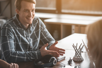 Portrait of young man talking to friends while sitting. Headphones on table