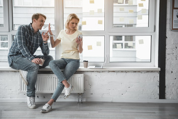 Man and woman with coffee cups taking seats at the window. Angry girl showing to guy silence gesture while concentrated on her smartphone. Copy space in right side