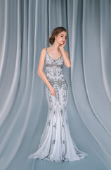 A young girl in a luxurious gray, -silver, sparkling, evening dress posing on the camera. Prom. Stylish bride in rustic style.