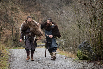 two Viking warriors walk on an ancient forest path