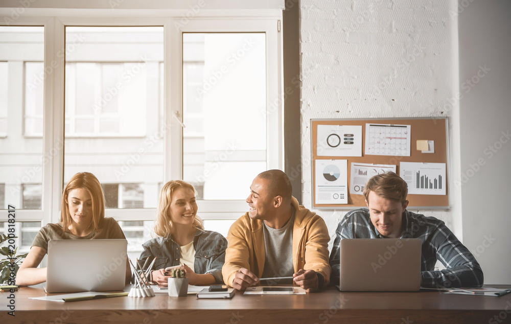 Fototapete men and women talking, using notebooks and smiling while sitting at desk. window and board with grap