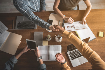 Top view of men and women having common work at desk. Guys are shaking hands. Close up