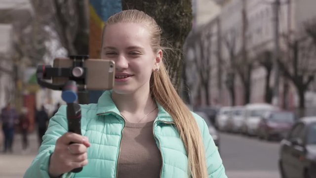 Girl vlogger with mobile phone camera stabilizer making videos for vlog. Travel vlogging equipment and gear. Teenage girl blogger recording new outdoor video in front of smartphone.