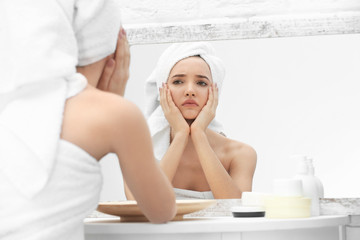 Teenage girl with acne problem looking in mirror indoors