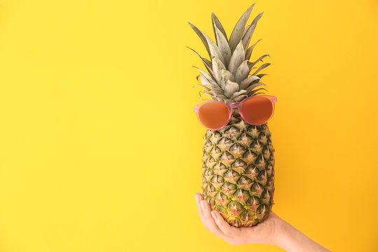 Woman holding fresh ripe pineapple with sunglasses on color background