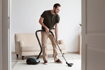 Young man cleaning carpet with vacuum in living room