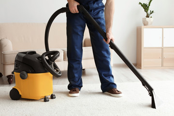 Male worker cleaning carpet with vacuum in living room