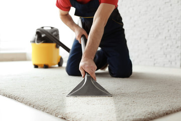 Male worker cleaning carpet with vacuum indoors
