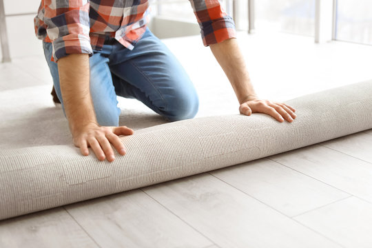 Man Rolling Out New Carpet Flooring In Room