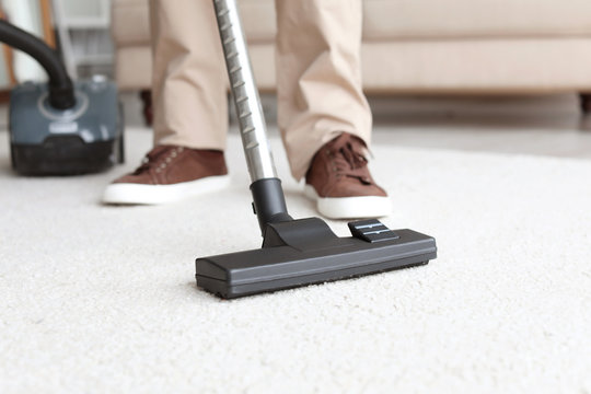 Man cleaning carpet with vacuum in living room