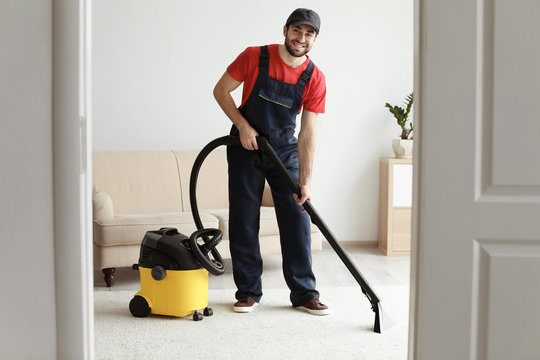 Male worker cleaning carpet with vacuum in living room