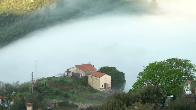 Early foggy morning in the Alpine town. Fog from the mountains makes its way along the medieval streets. Perinaldo, Liguria, Italy.