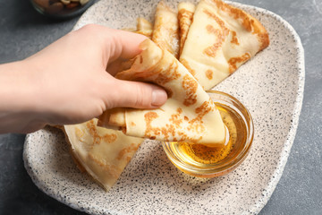 Woman dipping thin pancake into bowl with honey, closeup