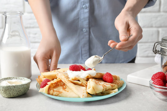 Woman adding sour cream to thin pancakes with berries at table