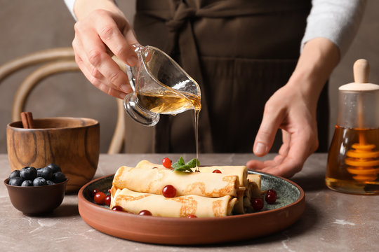 Woman pouring honey onto thin pancakes with berries at table