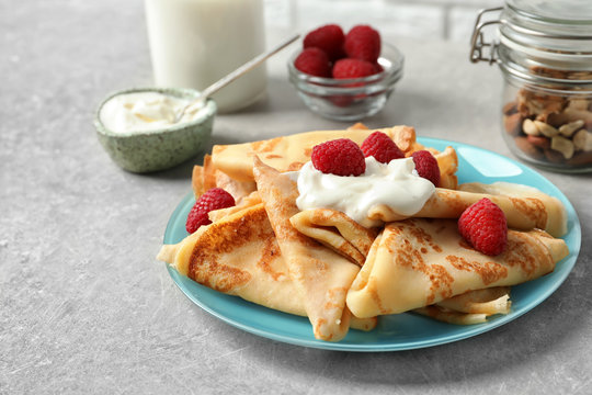 Thin pancakes with berries and sour cream on plate, closeup