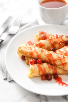 Thin pancakes with berries and syrup on plate, closeup