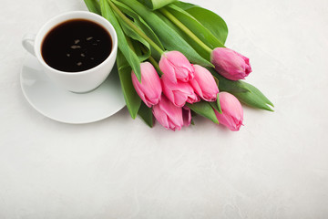 Black coffee in white Cup with pink tulips on light stone background. Top view with copy space