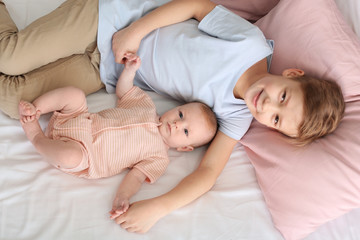 Cute little baby with elder brother lying on bed at home